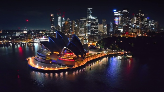 Aerial view of the Sydney Opera House illuminated at night with the city skyline in the background in Sydney New South Wales Australia. Aerial view of the Sydney Opera House illuminated at night with the city skyline in the background in Sydney New South Wales Australia.