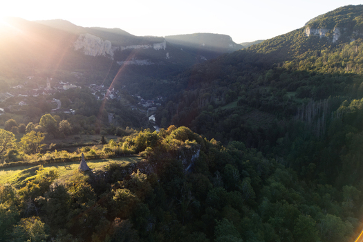 Aerial view of the historic village of Mouthier Haute Pierre nestled in a lush valley with rocky cliffs and a winding river during golden hour Lods Bourgogne Franche Comte France.
