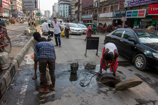 Dhaka Bangladesh 18 April 2018 View of workers cleaning a manhole on a busy city street with traffic and pedestrians in the background. Dhaka Bangladesh 18 April 2018 View of workers cleaning a manhole on a busy city street with traffic and pedestrians in the background.