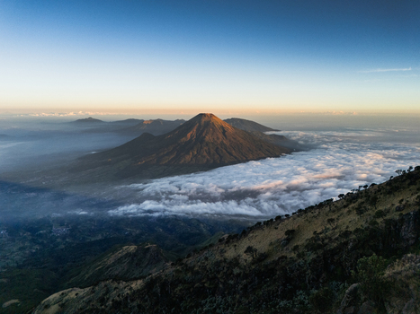 Aerial view of Gunung Sumbing rising above a sea of clouds during golden hour in Kecamatan Kalikajar Jawa Tengah Indonesia.