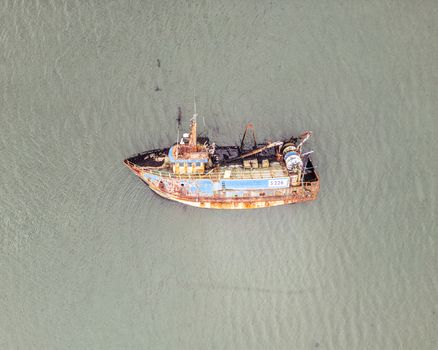 Aerial view of a rusty blue and orange fishing trawler floating on calm murky water. Aerial view of a rusty blue and orange fishing trawler floating on calm murky water.