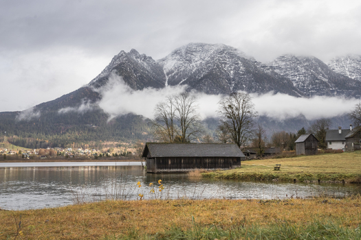 View of a wooden boathouse on the shore of a calm lake with snow capped mountains and low clouds in the background Hallstatt Upper Austria Austria. View of a wooden boathouse on the shore of a calm lake with snow capped mountains and low clouds in the background Hallstatt Upper Austria Austria.