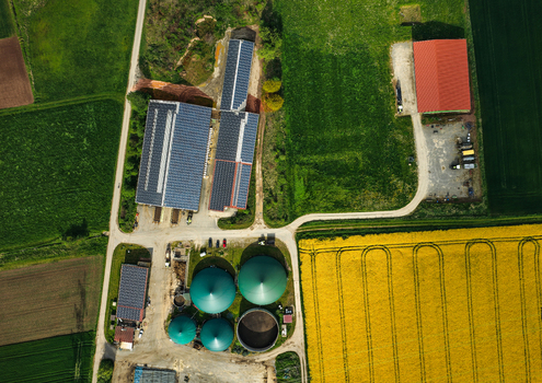 Aerial view of a modern farm complex with solar panels on rooftops and green biogas silos next to a vibrant yellow rapeseed field Hofgeismar Hessen Germany. Aerial view of a modern farm complex with solar panels on rooftops and green biogas silos next to a vibrant yellow rapeseed field Hofgeismar Hessen Germany.