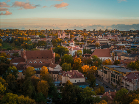 Aerial view of the old town with its terracotta rooftops and baroque churches amidst a tapestry of autumn foliage under a soft golden sky Vilnius Lithuania. Aerial view of the old town with its terracotta rooftops and baroque churches amidst a tapestry of autumn foliage under a soft golden sky Vilnius Lithuania.