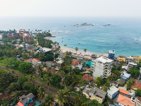Aerial view of the tropical coastline along the Indian Ocean with sandy beaches turquoise waters palm trees and rooftops Hikkaduwa Southern Province Sri Lanka. Aerial view of the tropical coastline along the Indian Ocean with sandy beaches turquoise waters palm trees and rooftops Hikkaduwa Southern Province Sri Lanka.