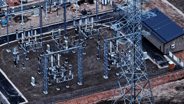 Aerial view of an electrical substation featuring high voltage power lines metal support structures transformers and a small utility building within a fenced compound in Latvia. Aerial view of an electrical substation featuring high voltage power lines metal support structures transformers and a small utility building within a fenced compound in Latvia.