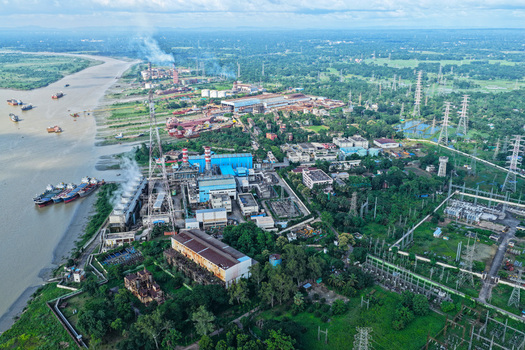 Aerial view of the Karnaphuli River with an industrial power plant cargo ships docked along the bank and lush green landscape in Chattogram Chittagong Division Bangladesh.