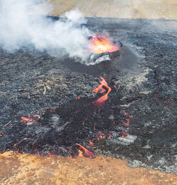 Aerial view of active volcanic eruption with glowing lava flowing from the crater across the dark solidified lava field in Iceland. Aerial view of active volcanic eruption with glowing lava flowing from the crater across the dark solidified lava field in Iceland.