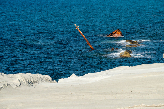 View of the shipwreck at Sarakiniko beach with its rusted mast protruding from the deep blue Aegean sea set against the iconic white volcanic rock formations of Milos Greece. View of the shipwreck at Sarakiniko beach with its rusted mast protruding from the deep blue Aegean sea set against the iconic white volcanic rock formations of Milos Greece.