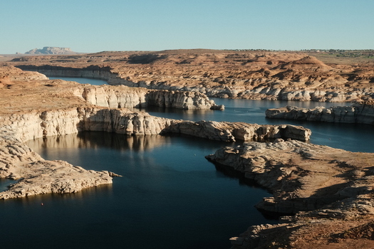 View of the deep blue water of Lake Powell winding through steep sandstone cliffs and arid desert landscape under a clear sky Lake Powell Arizona United States.