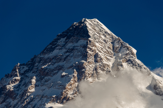 View of the majestic snow covered peak of K2 rising against a deep blue sky with clouds at the base in Concordia k2 Base Gilgit Baltistan Pakistan. View of the majestic snow covered peak of K2 rising against a deep blue sky with clouds at the base in Concordia k2 Base Gilgit Baltistan Pakistan.