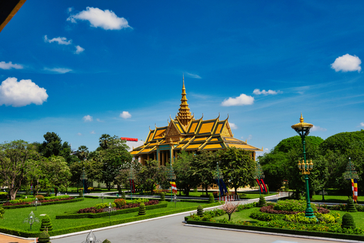 View of the Royal Palace of Cambodia featuring golden tiered roofs and ornate architecture surrounded by lush manicured gardens under a clear blue sky in Phnom Penh Phnom Penh Cambodia. View of the Royal Palace of Cambodia featuring golden tiered roofs and ornate architecture surrounded by lush manicured gardens under a clear blue sky in Phnom Penh Phnom Penh Cambodia.