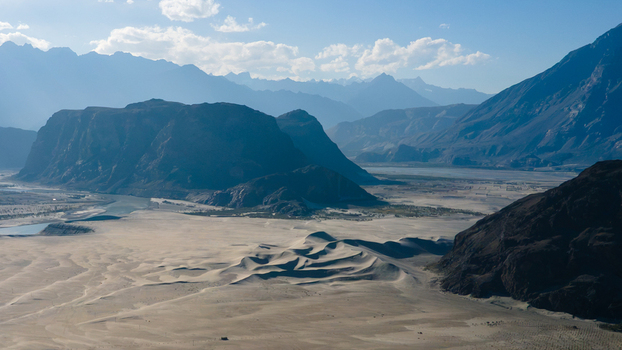 Aerial view of Sarfaranga Cold Desert Shigar with expansive sand dunes rugged mountain ranges and a winding river under a clear blue sky in Skardu Gilgit Pakistan. Aerial view of Sarfaranga Cold Desert Shigar with expansive sand dunes rugged mountain ranges and a winding river under a clear blue sky in Skardu Gilgit Pakistan.