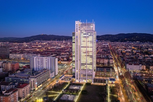 Aerial view of the Intesa Sanpaolo Skyscraper illuminated at dusk with the city skyline and distant mountains under a deep blue sky Torino Piemonte Italy. Aerial view of the Intesa Sanpaolo Skyscraper illuminated at dusk with the city skyline and distant mountains under a deep blue sky Torino Piemonte Italy.