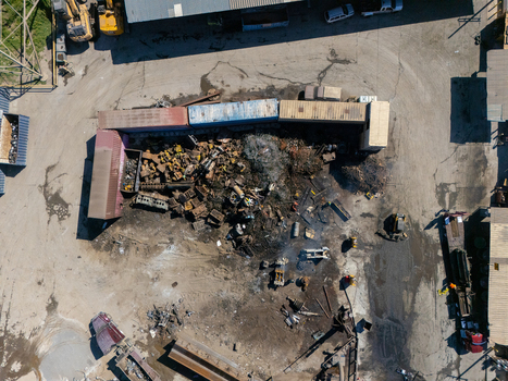 Aerial view of a scrap metal recycling facility featuring piles of discarded metal heavy machinery and shipping containers on a dirt lot in Carson California United States.