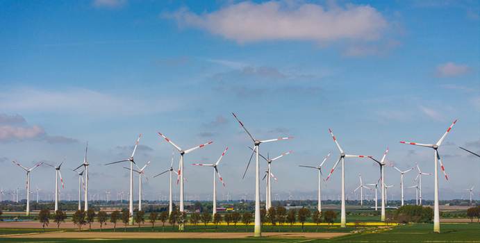 Aerial view of rows of wind turbines standing in a green agricultural field under a blue sky in Germany. Aerial view of rows of wind turbines standing in a green agricultural field under a blue sky in Germany.