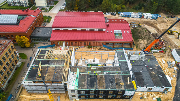 Aerial view of a construction site featuring a large building with a red roof scaffolding and workers active on the structure in Latvia. Aerial view of a construction site featuring a large building with a red roof scaffolding and workers active on the structure in Latvia.