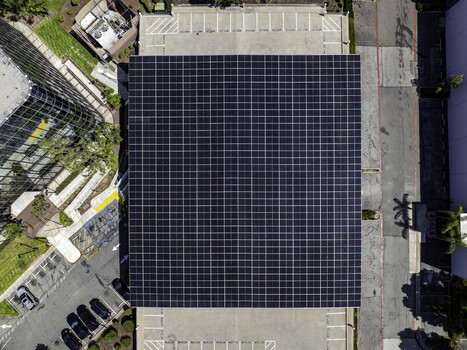 Aerial view of a large square solar panel array installed on a rooftop with surrounding parking lot and office building in Long Beach California United States. Aerial view of a large square solar panel array installed on a rooftop with surrounding parking lot and office building in Long Beach California United States.