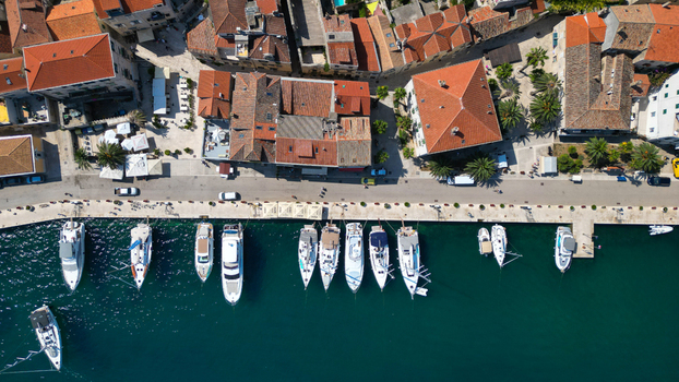 Aerial view of white yachts moored at the stone pier alongside historic terracotta rooftops and palm trees in Vis Split Dalmatia County Croatia. Aerial view of white yachts moored at the stone pier alongside historic terracotta rooftops and palm trees in Vis Split Dalmatia County Croatia.
