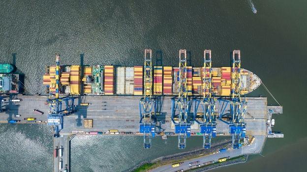 Aerial view of Jawaharlal Nehru Port Authority with a large container ship docked at the pier featuring colorful shipping containers and loading cranes in Juna Sheva Maharashtra India. Aerial view of Jawaharlal Nehru Port Authority with a large container ship docked at the pier featuring colorful shipping containers and loading cranes in Juna Sheva Maharashtra India.
