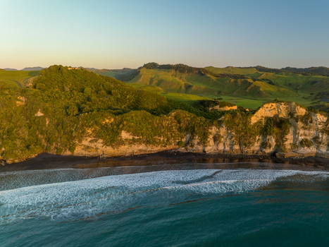 Aerial view of the rugged coastline where the ocean meets the dramatic cliffs bathed in the warm glow of the setting sun Waikawau Waikato Region New Zealand. Aerial view of the rugged coastline where the ocean meets the dramatic cliffs bathed in the warm glow of the setting sun Waikawau Waikato Region New Zealand.