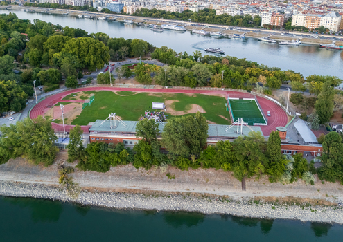 Aerial view of the athletics track on Margaret Island beside the Danube River with leafy parkland riverboats and the Budapest cityscape in summer evening light. Aerial view of the athletics track on Margaret Island beside the Danube River with leafy parkland riverboats and the Budapest cityscape in summer evening light.