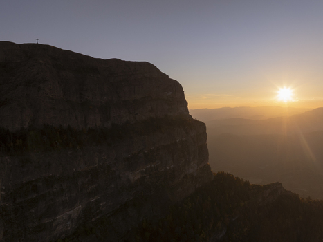 Aerial view of the Pyrenees mountain range at sunset featuring a prominent cliff face with a cross on the summit and warm golden light Spain. Aerial view of the Pyrenees mountain range at sunset featuring a prominent cliff face with a cross on the summit and warm golden light Spain.