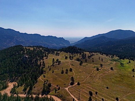 Aerial view of the Crescent Meadows Trailhead area with winding dirt trails pine forests and rolling mountain terrain under a clear blue sky in Golden Colorado United States. Aerial view of the Crescent Meadows Trailhead area with winding dirt trails pine forests and rolling mountain terrain under a clear blue sky in Golden Colorado United States.