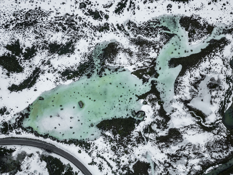 Aerial view of Grotfjord featuring turquoise frozen waters surrounded by snow covered rocky terrain and a winding road in Tromvik Troms Norway. Aerial view of Grotfjord featuring turquoise frozen waters surrounded by snow covered rocky terrain and a winding road in Tromvik Troms Norway.