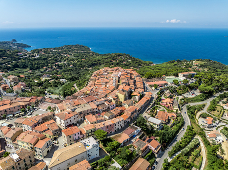 Aerial view of the historic hilltop town of Capoliveri with dense terracotta rooftops and narrow streets surrounded by lush vegetation overlooking the sea in Capoliveri Tuscany Italy.