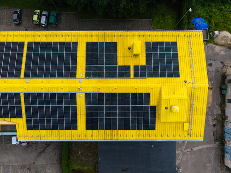 Aerial view of a bright yellow industrial roof covered with rows of dark solar panels featuring a metal ladder and surrounding paved parking area in Valdlauci Kekava Municipality Latvia. Aerial view of a bright yellow industrial roof covered with rows of dark solar panels featuring a metal ladder and surrounding paved parking area in Valdlauci Kekava Municipality Latvia.