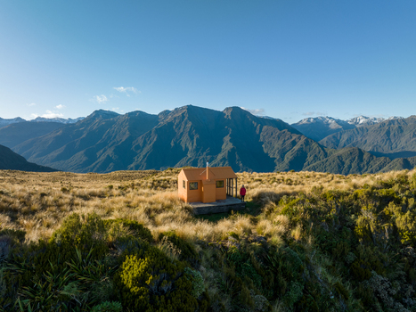 Aerial view of a solitary orange hut standing proudly amidst a vast expanse of golden tussock grass with rugged mountains in the backdrop Lake Kaniere West Coast Region New Zealand. Aerial view of a solitary orange hut standing proudly amidst a vast expanse of golden tussock grass with rugged mountains in the backdrop Lake Kaniere West Coast Region New Zealand.