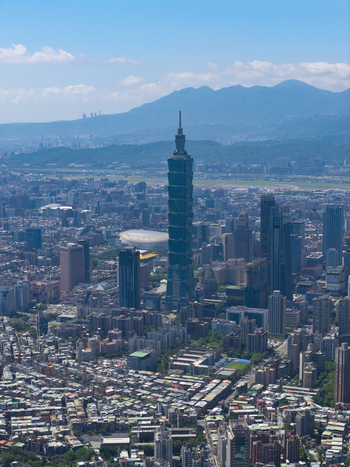 Aerial view of Taipei 101 skyscraper rising above the dense urban landscape surrounded by residential buildings commercial towers and distant mountains under a clear blue sky Taipei City Taiwan. Aerial view of Taipei 101 skyscraper rising above the dense urban landscape surrounded by residential buildings commercial towers and distant mountains under a clear blue sky Taipei City Taiwan.