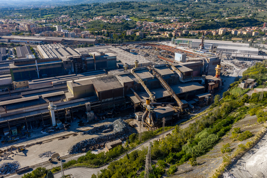 Aerial view of Acciai Speciali Terni S.p.A. steel plant with large industrial buildings metal scrap piles and surrounding greenery in Terni Umbria Italy.