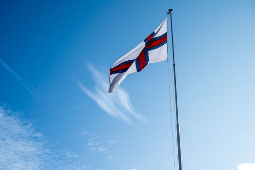 View of the flag of the Faroe Islands waving against a clear blue sky in the Faroe Islands. View of the flag of the Faroe Islands waving against a clear blue sky in the Faroe Islands.