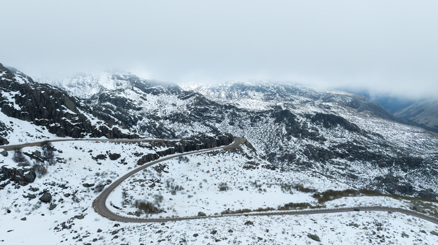 Aerial view of Glacial Valley Deck and a winding mountain road cutting through a snow covered landscape with rocky peaks in Loriga Guarda District Portugal. Aerial view of Glacial Valley Deck and a winding mountain road cutting through a snow covered landscape with rocky peaks in Loriga Guarda District Portugal.