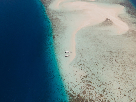 Aerial view of Pasir Timbul Mansuar sandbar surrounded by turquoise coral reefs and deep blue ocean waters with small boats anchored in Raja Ampat Papua Barat Indonesia. Aerial view of Pasir Timbul Mansuar sandbar surrounded by turquoise coral reefs and deep blue ocean waters with small boats anchored in Raja Ampat Papua Barat Indonesia.
