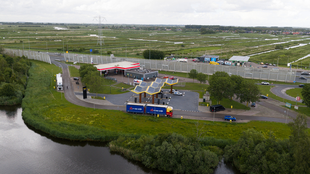 Oostzaan Netherlands 09 June 2026 Aerial view of the Fastned charging station featuring a distinctive solar panel roof situated near a highway green fields and a canal.