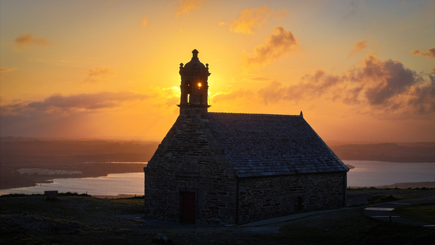 Aerial view of Chapelle Saint Michel de Brasparts silhouetted against a golden sunset with the sun glowing through the bell tower in Saint Rivoal Bretagne France. Aerial view of Chapelle Saint Michel de Brasparts silhouetted against a golden sunset with the sun glowing through the bell tower in Saint Rivoal Bretagne France.