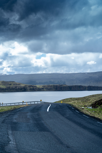 View of a winding asphalt road leading towards the Hvalfjordur fjord under a dramatic cloudy sky in Iceland. View of a winding asphalt road leading towards the Hvalfjordur fjord under a dramatic cloudy sky in Iceland.