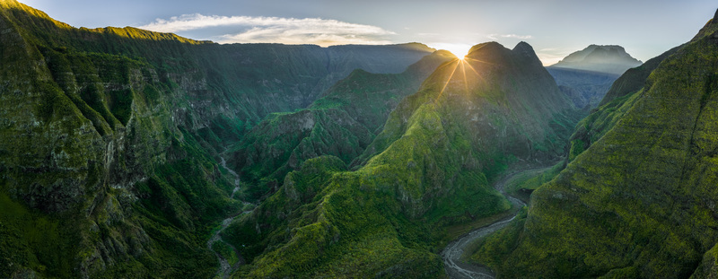 Aerial view of the lush volcanic valley with steep green ridges and a winding river during a golden sunrise La Reunion France. Aerial view of the lush volcanic valley with steep green ridges and a winding river during a golden sunrise La Reunion France.