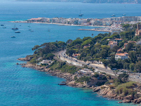 Aerial view of the coastline of Antibes featuring the Mediterranean Sea rocky cliffs a coastal road lush pine trees and the urban skyline in Antibes Provence Alpes Cote d Azur France. Aerial view of the coastline of Antibes featuring the Mediterranean Sea rocky cliffs a coastal road lush pine trees and the urban skyline in Antibes Provence Alpes Cote d Azur France.