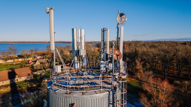 Valmiera Latvia 11 November 2025 Aerial view of a telecommunications tower equipped with various antennas and satellite dishes set against a rural landscape with a lake and trees.