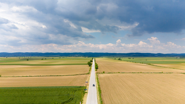 Aerial view of a straight asphalt road stretching through golden and green agricultural fields under a dramatic cloudy sky in Novi Sad Vojvodina Serbia. Aerial view of a straight asphalt road stretching through golden and green agricultural fields under a dramatic cloudy sky in Novi Sad Vojvodina Serbia.
