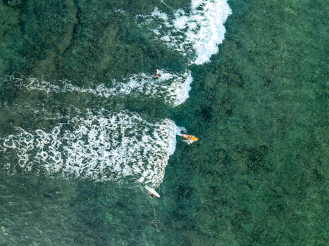 Aerial view of surfers riding waves on surfboards over a shallow coral reef at Mahaybo Beach in General Luna Caraga Philippines. Aerial view of surfers riding waves on surfboards over a shallow coral reef at Mahaybo Beach in General Luna Caraga Philippines.