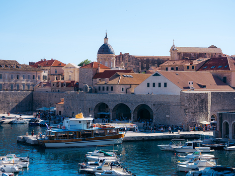 View of the historic harbor in Dubrovnik Old Town with boats moored near stone walls and red tiled rooftops under a clear blue sky in Dubrovnik Dubrovnik Neretva County Croatia. View of the historic harbor in Dubrovnik Old Town with boats moored near stone walls and red tiled rooftops under a clear blue sky in Dubrovnik Dubrovnik Neretva County Croatia.