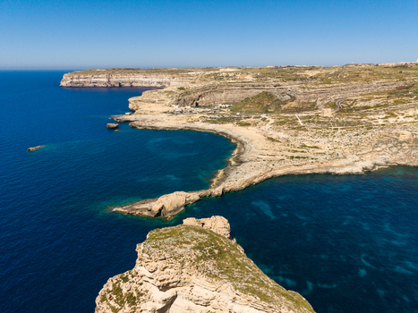 Aerial view of the rugged limestone cliffs and turquoise waters of Dwejra Bay along the rocky coastline under a clear blue sky in Gozo Region Malta. Aerial view of the rugged limestone cliffs and turquoise waters of Dwejra Bay along the rocky coastline under a clear blue sky in Gozo Region Malta.