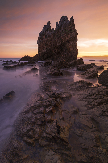 View of the jagged sea stacks at Playa de Portizuelo surrounded by misty ocean waves during a vibrant sunset Spain. View of the jagged sea stacks at Playa de Portizuelo surrounded by misty ocean waves during a vibrant sunset Spain.