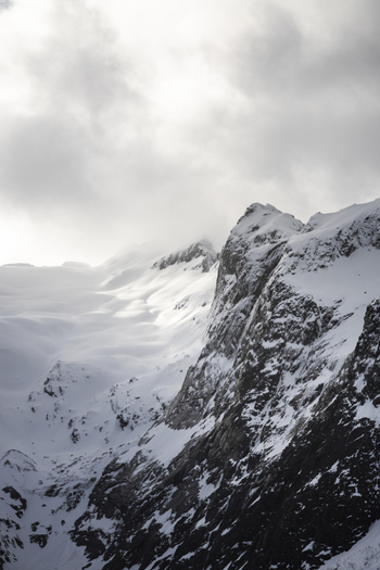 View of snow covered mountain peaks and rocky cliffs under a dramatic cloudy sky in the arctic landscape of Kvaloya Troms Norway. View of snow covered mountain peaks and rocky cliffs under a dramatic cloudy sky in the arctic landscape of Kvaloya Troms Norway.
