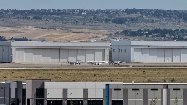 Aerial view of small aircraft parked on the tarmac in front of large white hangars with industrial buildings in the foreground in Centennial Colorado United States.